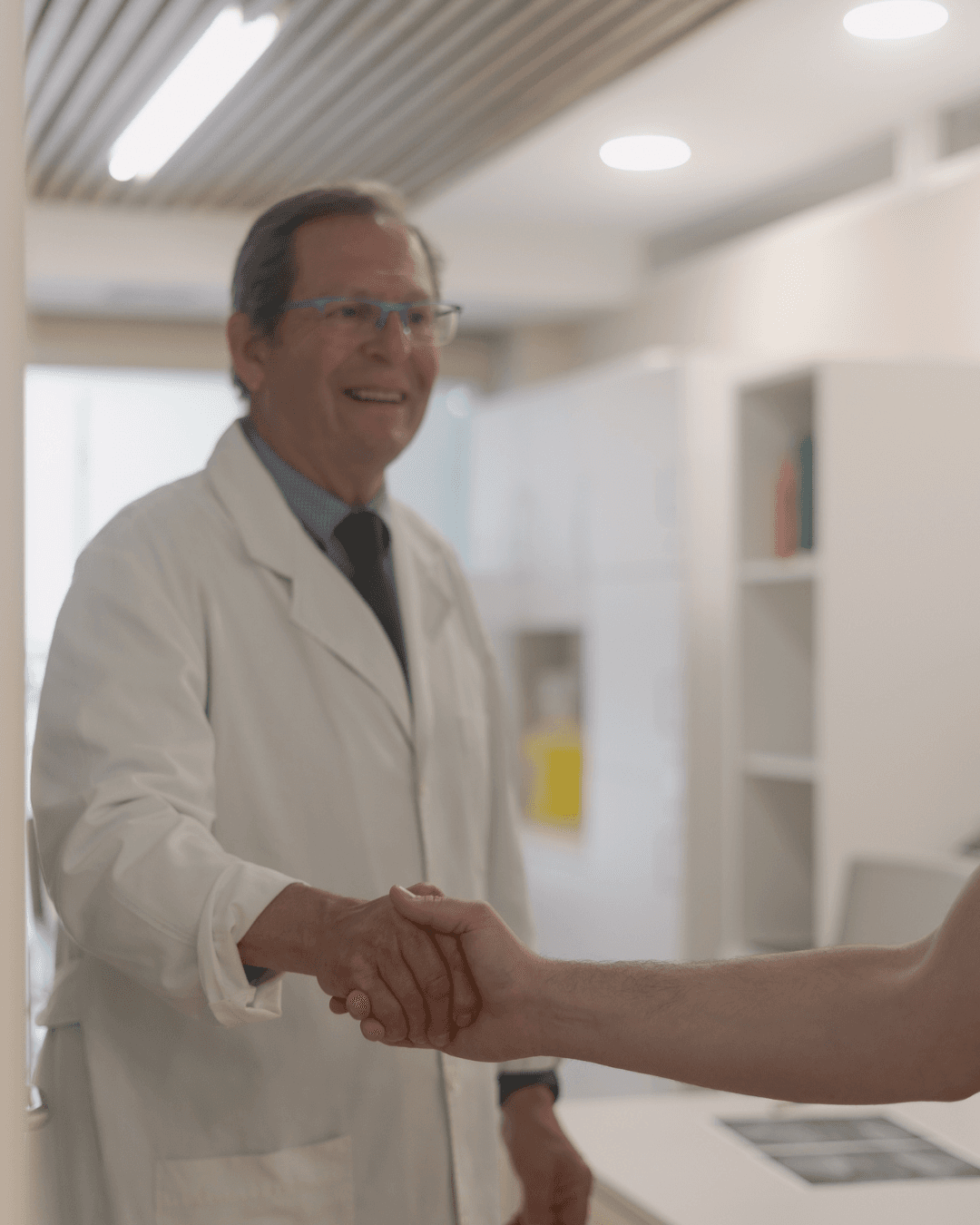 Médico sonriente con bata blanca estrecha la mano de un paciente en su consultorio.