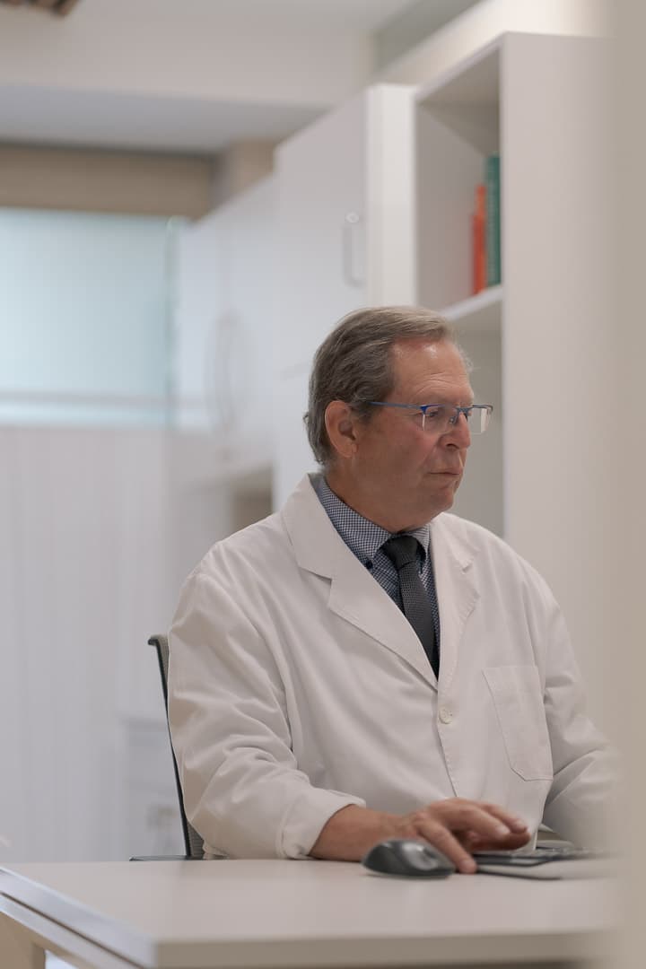 Médico mayor con gafas y bata blanca trabajando en su escritorio en un consultorio.