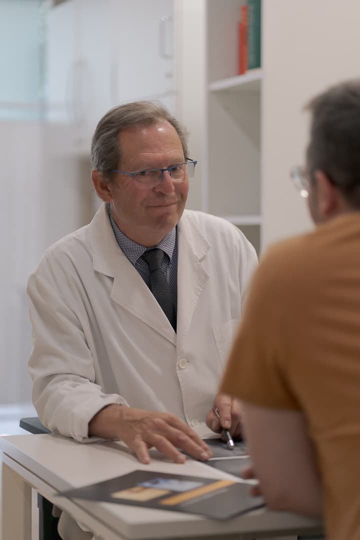 Doctor con bata blanca y gafas sonriendo durante una consulta médica con un paciente.