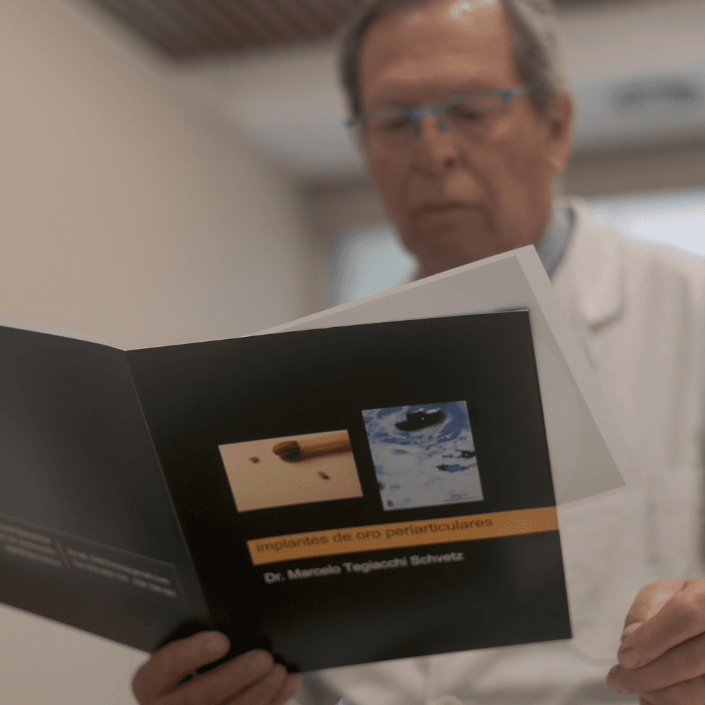 Médico leyendo un folleto sobre implantes de oro periarticulares del Dr. Marcelo Tegiacchi Schwetz.